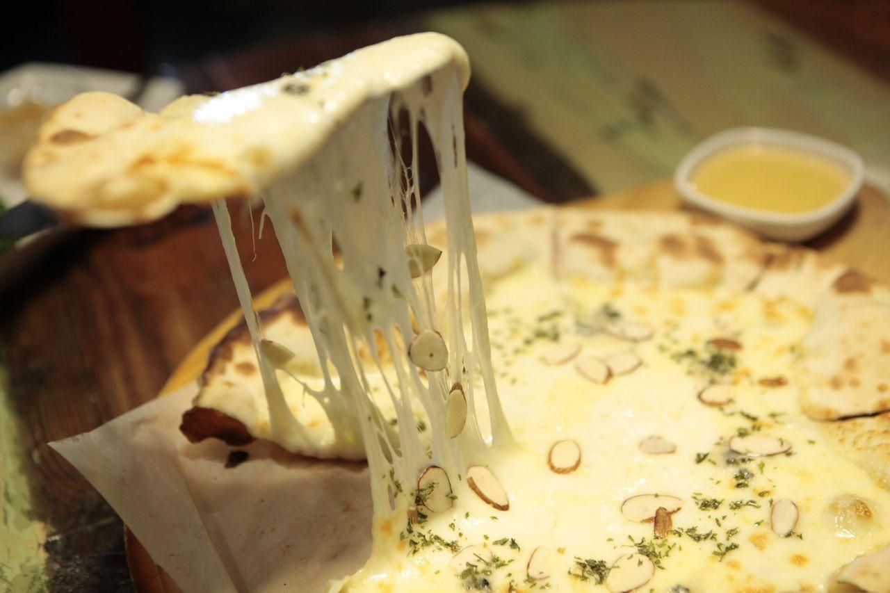 Close-up of a slice of Gorgonzola pizza being lifted, with a generous stretch of melted cheese and crunchy almond toppings.